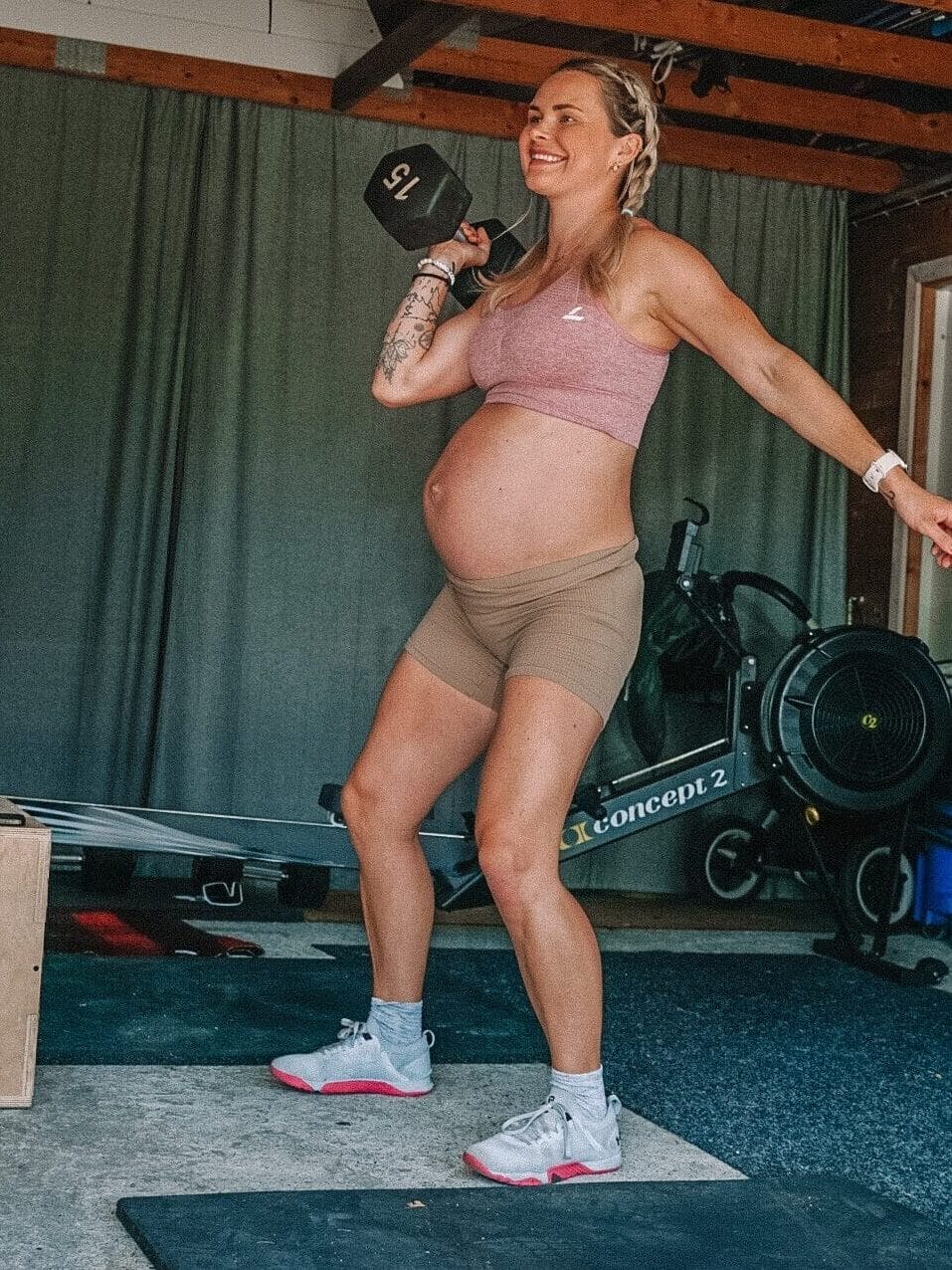 Gravid kvinne som trener skulderpress med en treningsmanual på 15 kg i høyre hånd